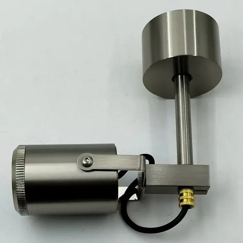 A brushed metal cylindrical mechanical component with a vertical rod, circular top plate, mounting bracket, black cable, and a small gold connector, photographed on a plain light background.
